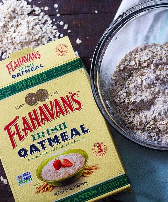 An overhead shot of a box of Flahavan\'s Irish Oatmeal with some of the dried oatmeal in a clear mixing bowl