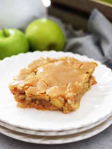 A slice of this fresh apple sheet cake on a white plate with green granny smith apples in the background