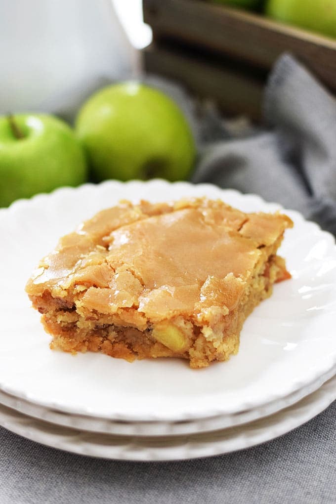 A slice of this fresh apple sheet cake on a white plate with green granny smith apples in the background