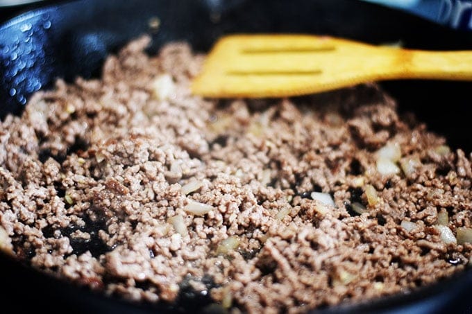 Browned ground beef and onions cooling in a black cast iron skillet with a wooden spoon in the background