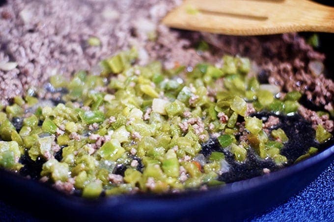 Green peppers sautéing in a black cast iron skillet with a ground beef and onions for this cheesy unstuffed pepper skillet