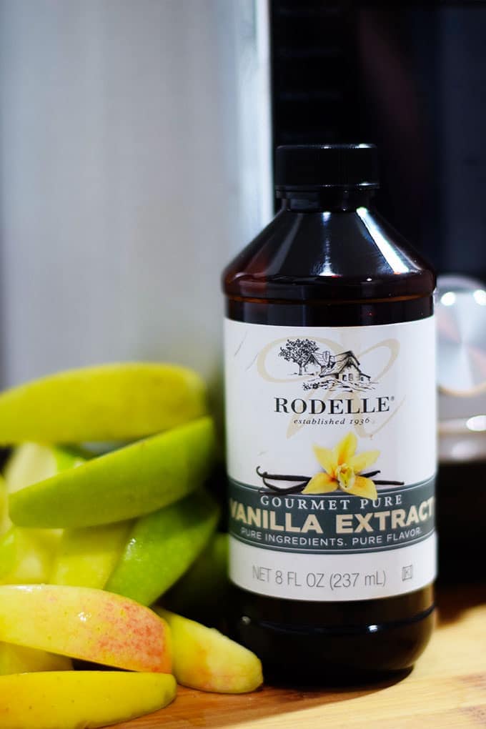 a closeup of Rodelle pure vanilla extract with sliced green apples in the background that was used in this instant pot apple butter recipe