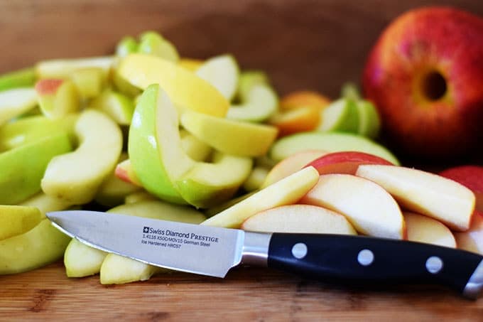 Sliced red and green apples on a wooden cutting board with a Swiss Diamond knife