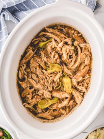 A white slow cooker filled with Mississippi Chicken