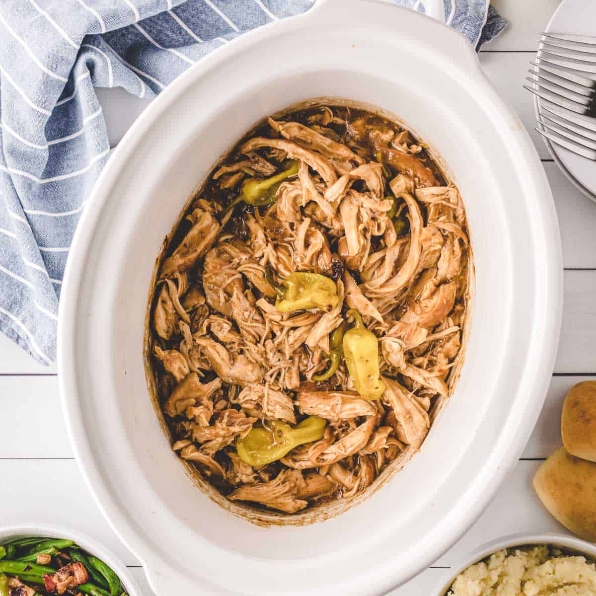 A white slow cooker filled with Mississippi Chicken