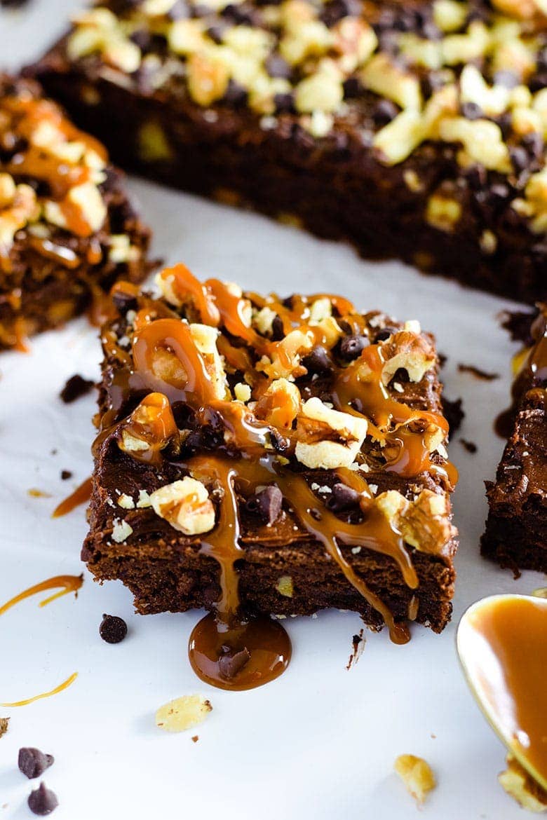 A closeup of a frosted chocolate turtle brownie with caramel and chopped pecans