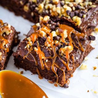 A closeup of this decadent chocolate turtle brownie topped with caramel, chocolate chips, and chopped nuts