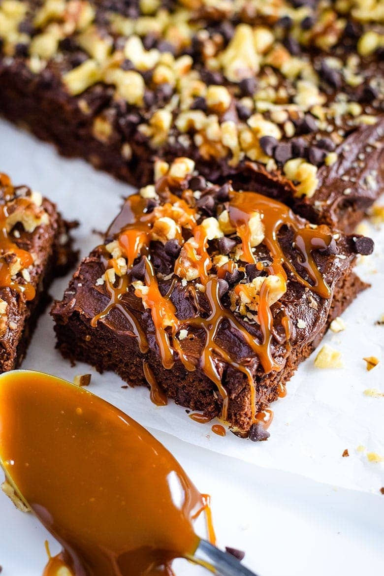 A closeup of this decadent chocolate turtle brownie topped with caramel, chocolate chips, and chopped nuts