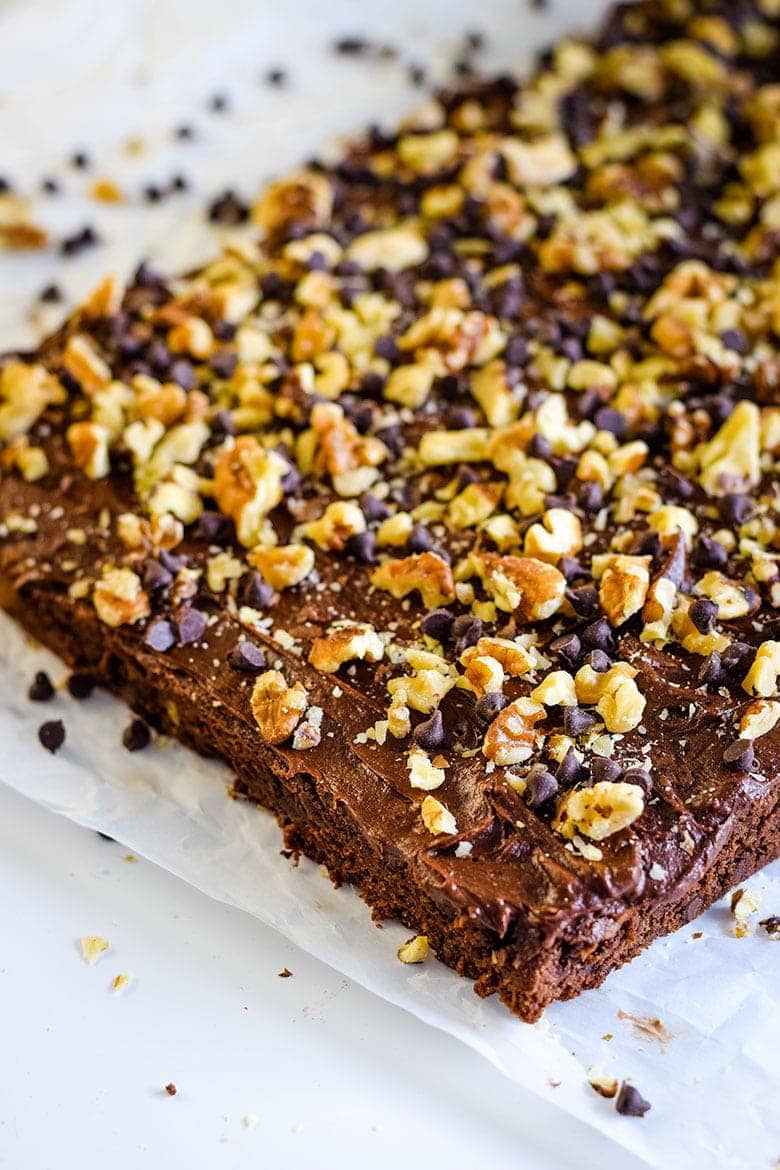 A closeup of these frosted chocolate turtle brownies with caramel and chopped pecans before they\'re sliced