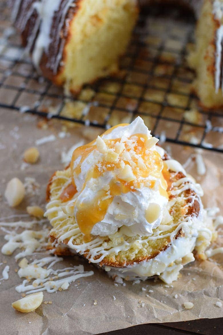 A slice of this white chocolate macadamia nut pound cake with icing, whipped cream, and shredded coconut