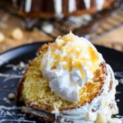 A slice of this white chocolate macadamia nut pound cake with icing, whipped cream, and shredded coconut