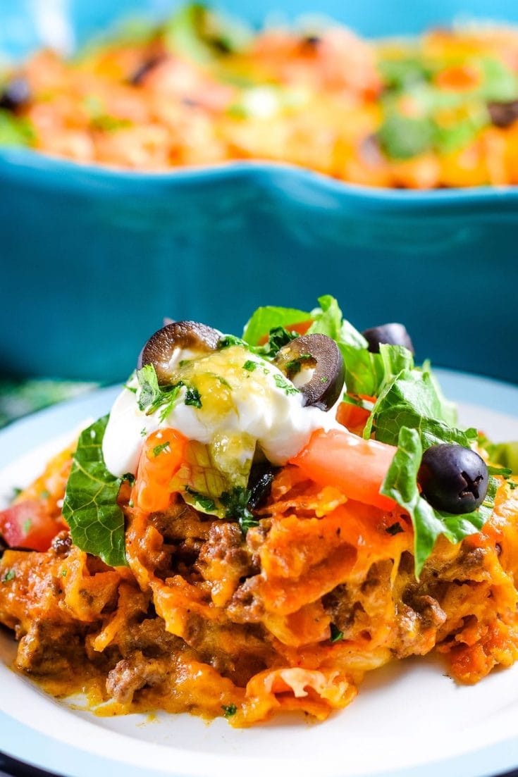 A closeup of this ground beef Doritos casserole with black olives, diced tomatoes, sour cream, and parsley