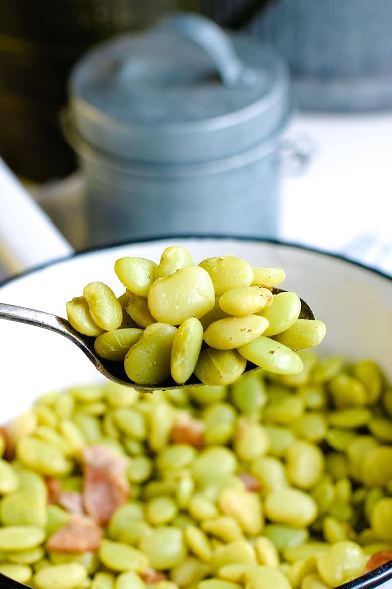 A ceramic cooking pot filled with these southern-style baby lime beans and a serving spoon with some ready for a bite