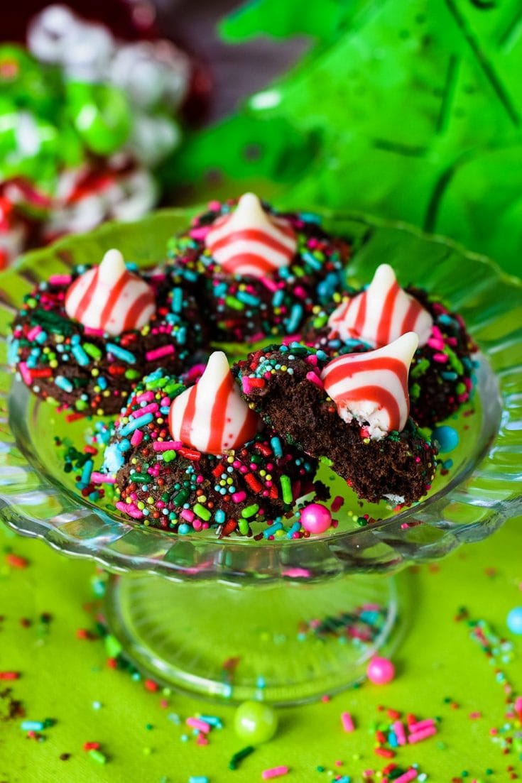 Several chocolate candy cane Hershey\'s kiss cookies with Christmas sprinkles on a glass platter
