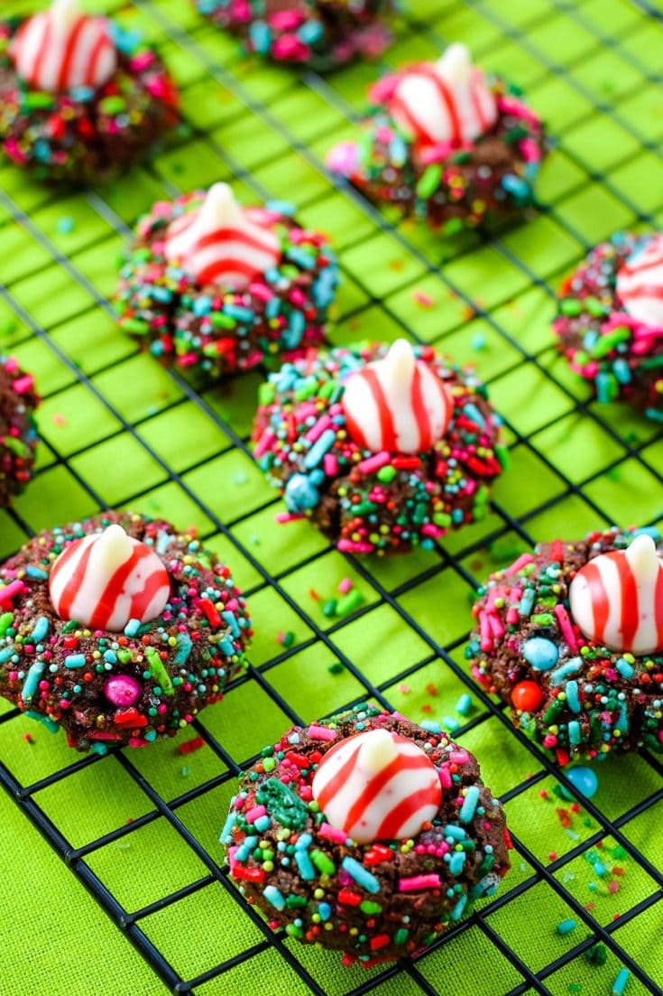 Several chocolate candy cane Hershey\'s kiss cookies with Christmas sprinkles on a wire rack