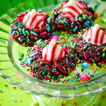 A close up of four chocolate candy cane Hershey's kiss cookies with Christmas sprinkles on a glass platter
