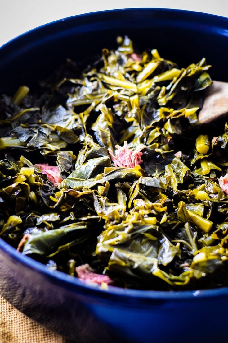 A large cooking pot filled with these southern collard greens and a wooden spoon