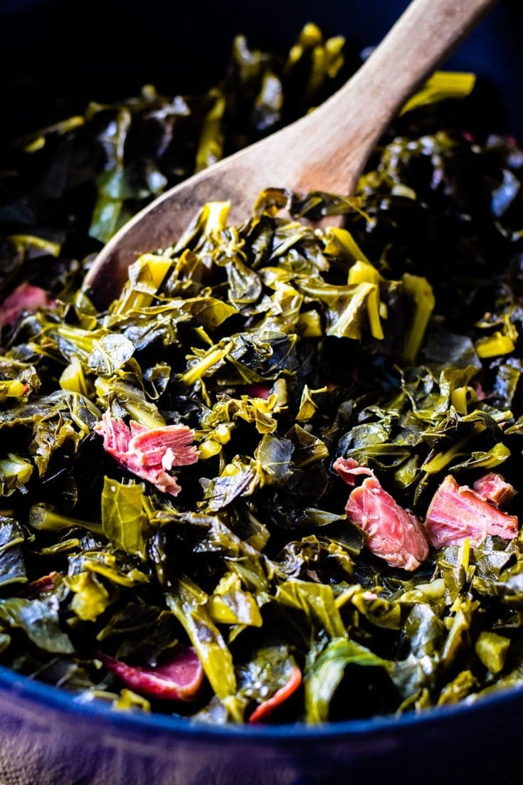 Pot of Southern Collard greens with a wooden spoon scooped full of greens.