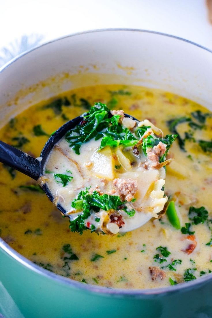 A large pot filled with this homemade Zuppa Toscana soup recipe with sausage and kale and a ladle of the soup in the foreground of the image