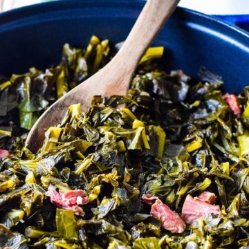 A large cooking pot filled with these southern collard greens and a wooden spoon