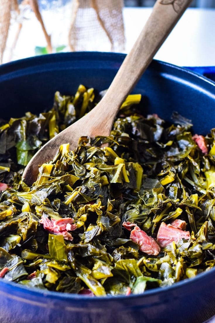 A large cooking pot filled with these southern collard greens and a wooden spoon