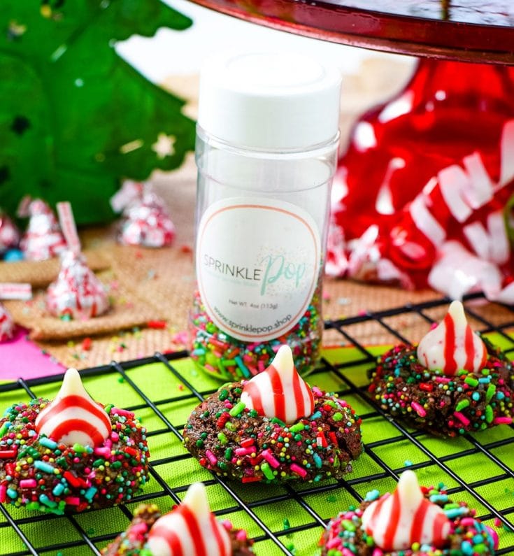 A close up of four chocolate candy cane Hershey\'s kiss cookies on a cooling rack with Christmas sprinkles 