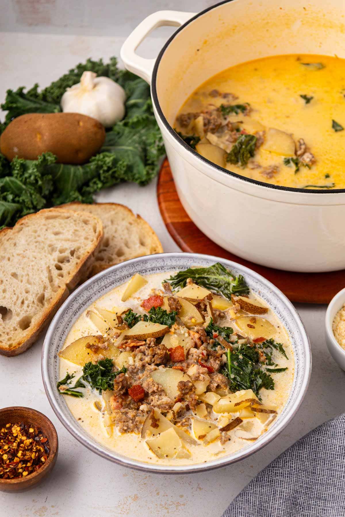 A bowl of Zuppa Toscana soup along with sliced crusty bread and  the dutch oven pot in the background.