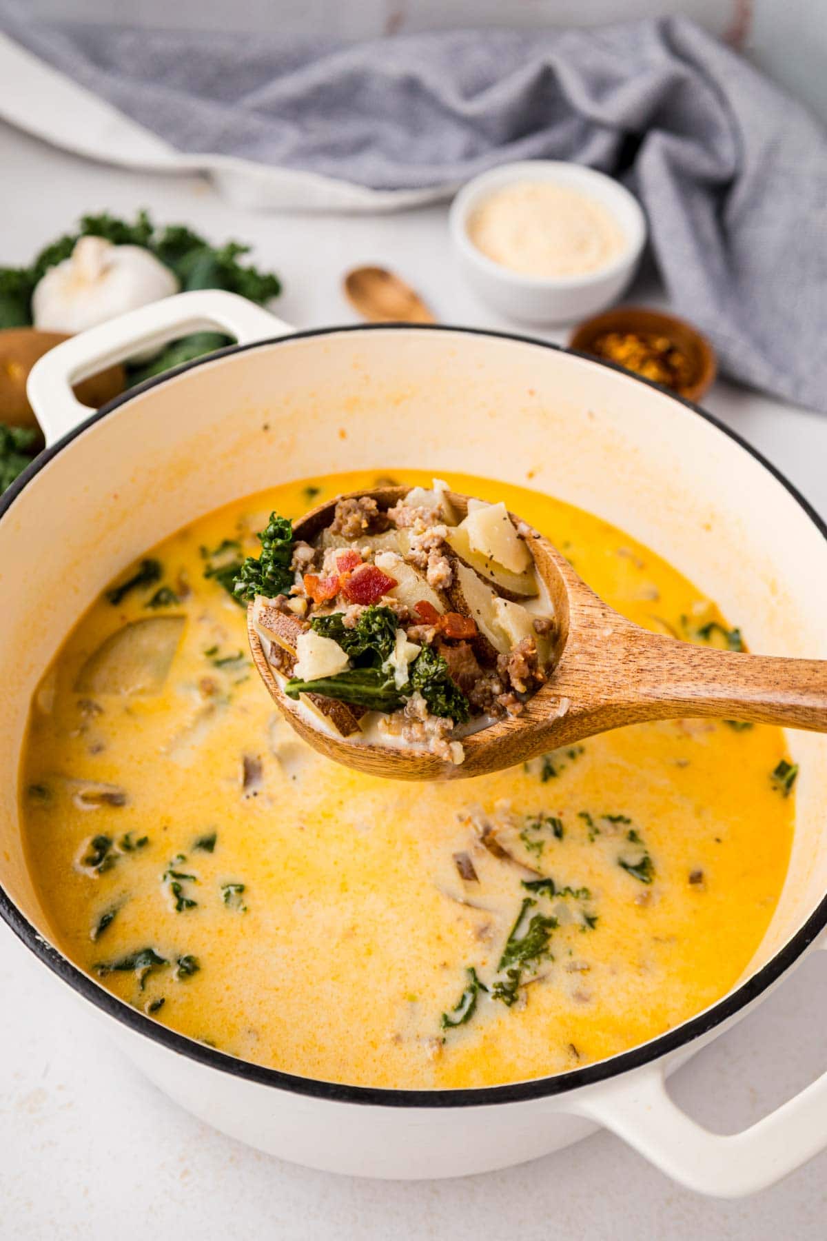 Zuppa Toscana soup being ladled with a wooden spoon from a white dutch oven. 