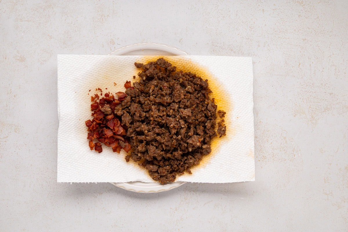 Sausage and bacon on a paper towel lined plate draining excess grease.