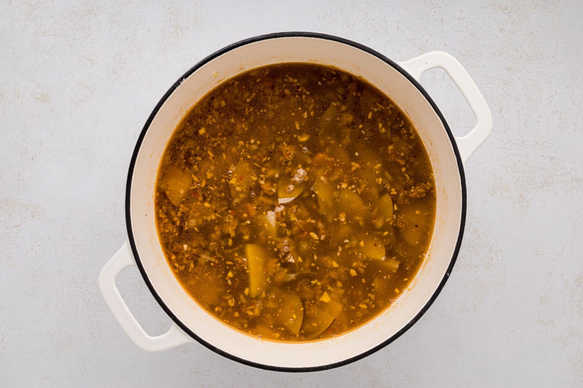 Meats, potatoes and spices stirred to combine in the soup pot.