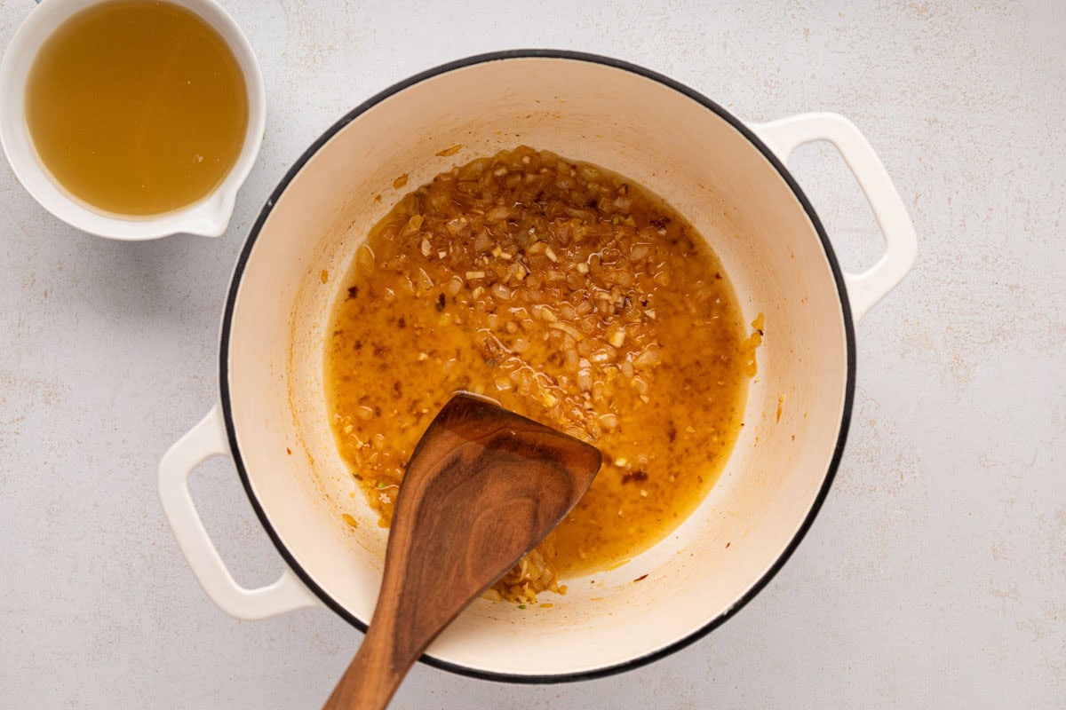 Using a wooden spatula to deglaze the bottom of the dutch oven with chicken stock.
