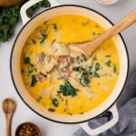 A white dutch oven filled with Zuppa Toscana soup with a wooden spoon in the soup.