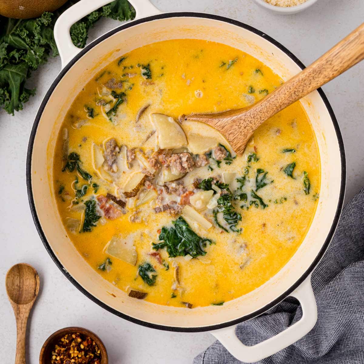 A white dutch oven filled with Zuppa Toscana soup with a wooden spoon in the soup.
