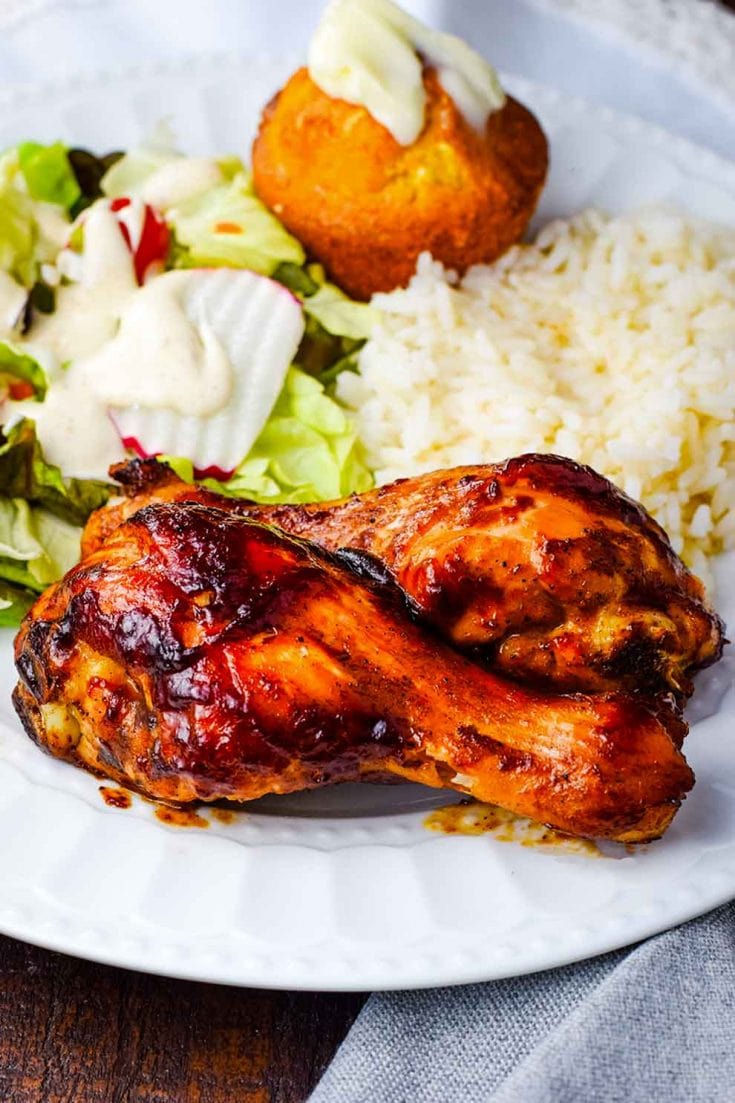 A plate served with a baked bbq chicken drumstick, white rice, cornbread, and a side salad