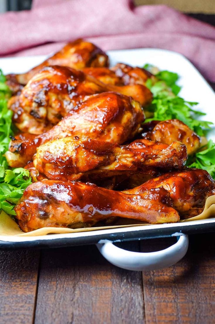 A serving dish filled with these oven baked barbecue chicken drumsticks with parsley as a garnish