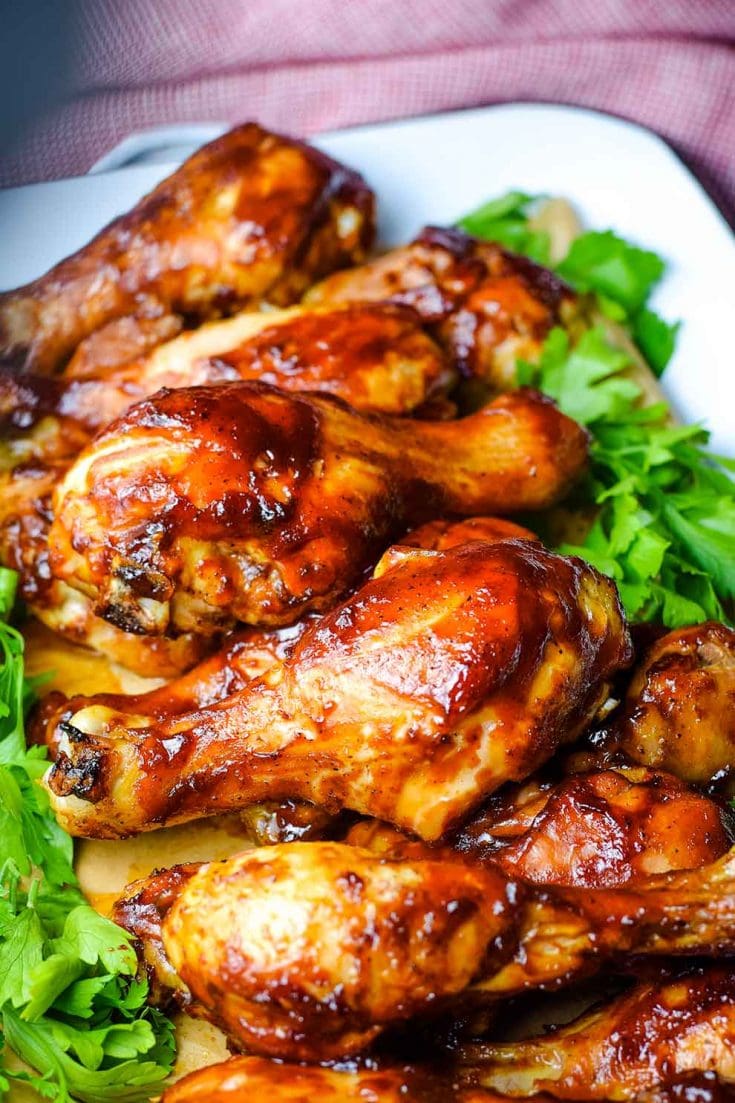 A serving dish filled with these oven baked barbecue chicken drumsticks with parsley as a garnish