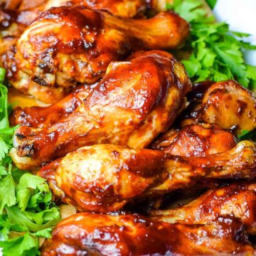 A serving dish filled with these oven baked barbecue chicken drumsticks with parsley as a garnish