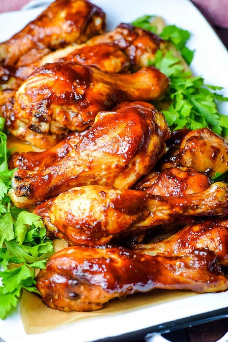 A serving dish filled with these oven baked barbecue chicken drumsticks with parsley as a garnish