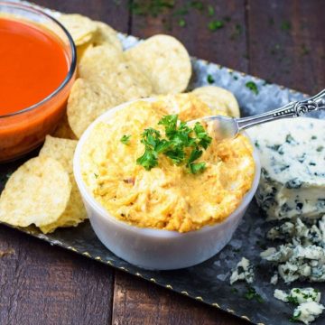 a serving platter with chips, buffalo sauce, crumbled blue cheese, and a white owl of this slow cooker buffalo chicken dip