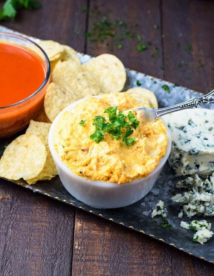 a serving platter with chips, buffalo sauce, crumbled blue cheese, and a white owl of this slow cooker buffalo chicken dip