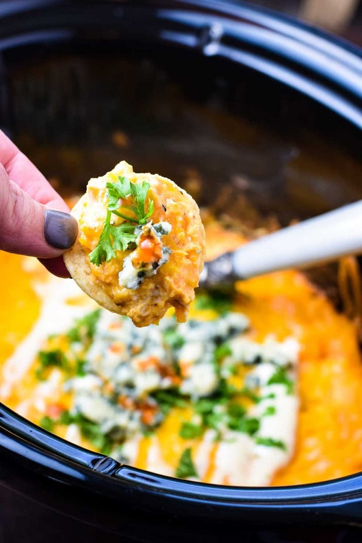 The chef dipping a tortilla chip in a slow cooker filled with this crock pot buffalo chicken dip to make the perfect game day appetizer