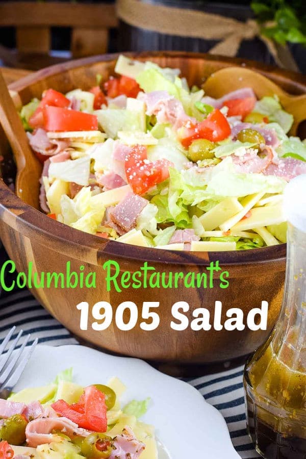 A large wooden serving bowl of this Columbia Restaurant\'s 1905 salad recipe topped with ham, green olives, and tomatoes Pinterest image