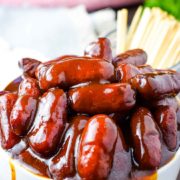 A white bowl filled with these crock pot barbecue little smokies smothered in bbq sauce with a cup of toothpicks for serving in the background