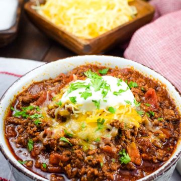 A bowl of this low-carb no-bean chili recipe topped with shredded cheese, sour cream, and parsley