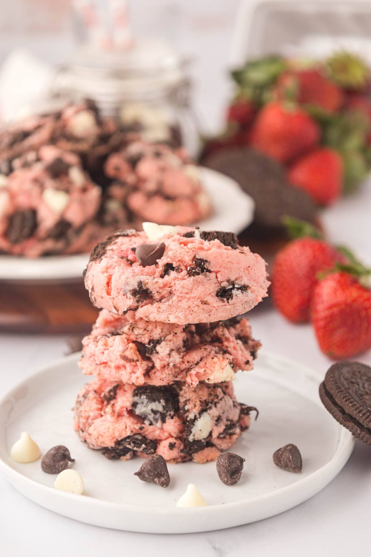 Three strawberry cheesecake Oreo cookies stacked on a plate with scattered chocolate chips.