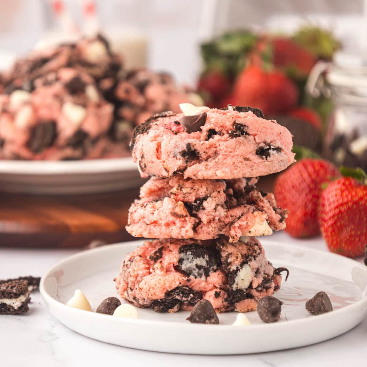 Three strawberry cheesecake Oreo cookies stacked on a plate with scattered chocolate chips.