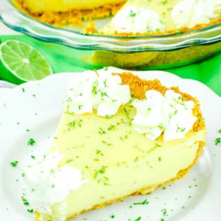 A slice of the best key lime pie on a white plate topped with whipped cream and lime zest