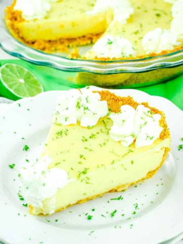 A slice of the best key lime pie on a white plate topped with whipped cream and lime zest