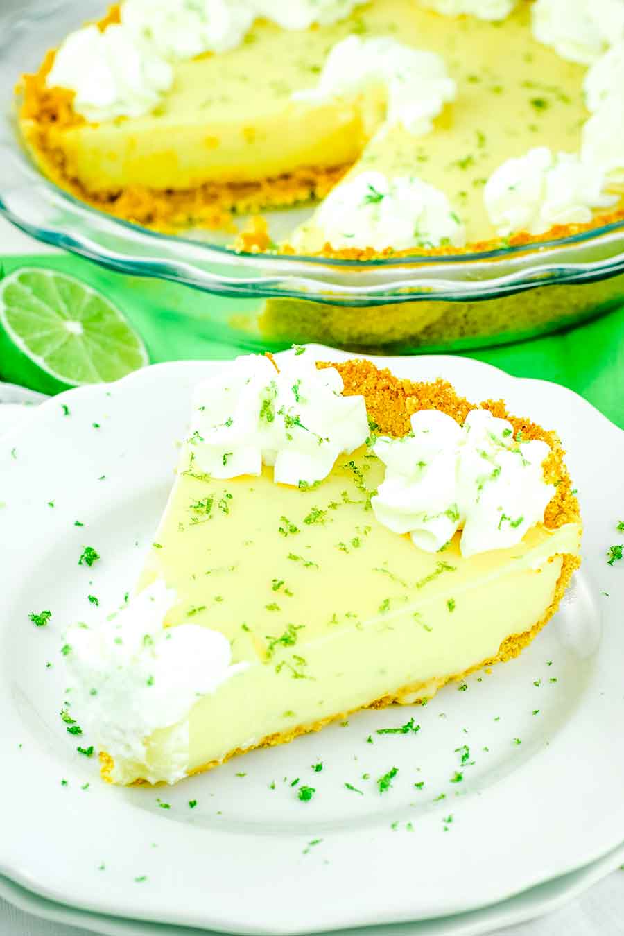 A slice of the best key lime pie on a white plate topped with whipped cream and lime zest