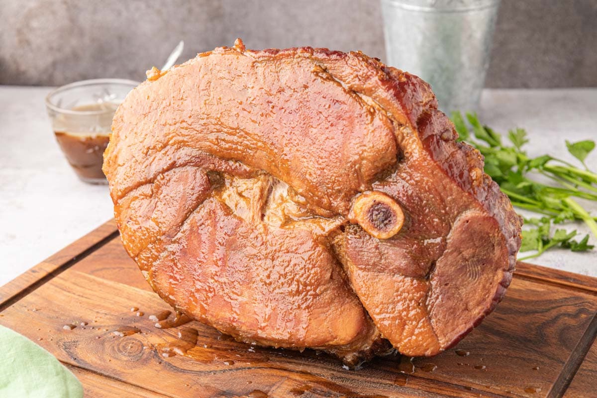 The whole ham on a cutting board with juices spooned over the top.